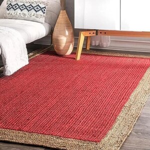 May include: A red jute rug with a natural jute border. The rug has a woven texture and is perfect for adding a touch of natural style to any room.
