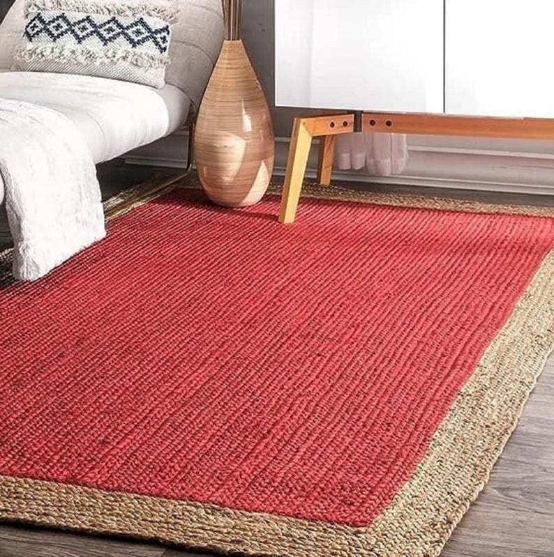 May include: A red jute rug with a natural jute border. The rug has a woven texture and is perfect for adding a touch of natural style to any room.