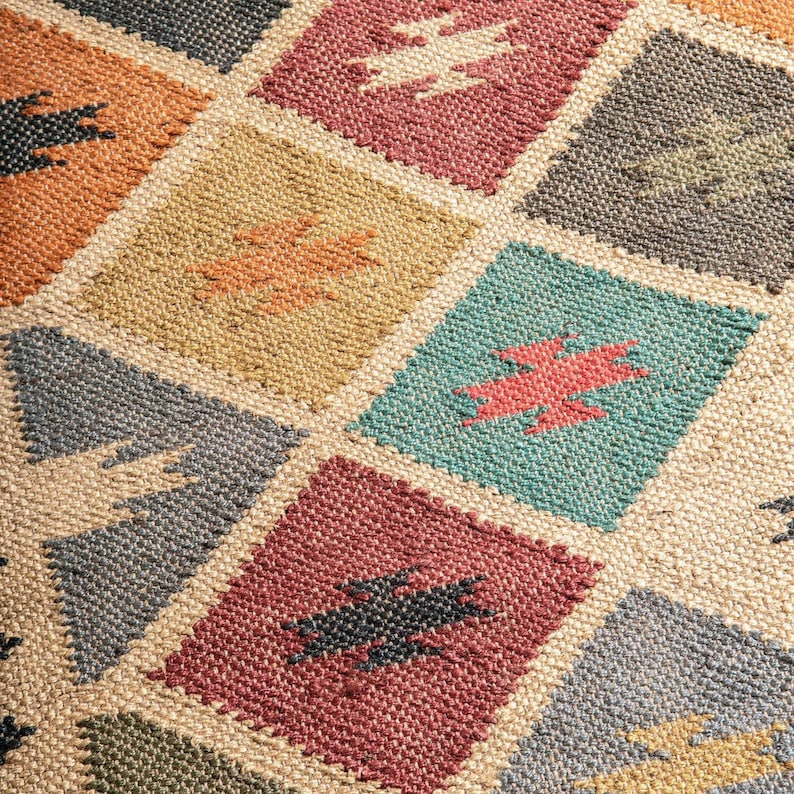 K&ouml;nnte beinhalten: Nahaufnahme eines gewebten Teppichs mit geometrischem Muster. Der Teppich weist ein sich wiederholendes Rautenmuster mit Quadraten in verschiedenen Farben auf, darunter Orange, Rot, T&uuml;rkis und Grau. Jedes Quadrat enth&auml;lt ein stilisiertes Blitzdesign.