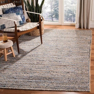 Puede incluir: Una alfombra de yute rayada en azul y beige con una textura de fibra natural. La alfombra se coloca en un salón con una silla de madera y un pequeño taburete.