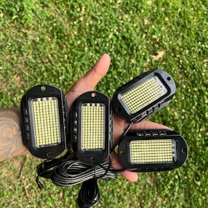 May include: Four black LED lights with a white grid of LEDs. The lights are connected by a black wire.