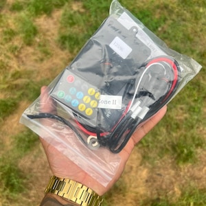 May include: A clear plastic bag containing a black electronic device, a remote control with colored buttons, and wires. The remote control has the text "Zone II" and "RF". The bag also has a white sticker with the number "12556".