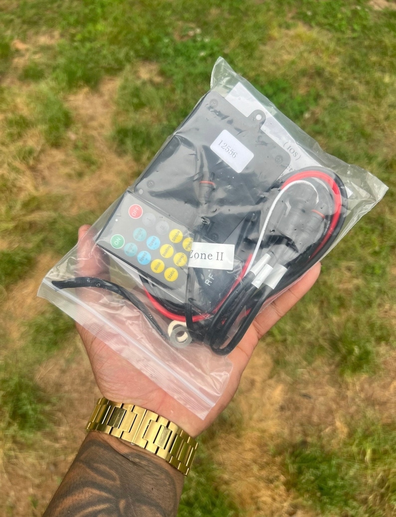 K&ouml;nnte beinhalten: Eine transparente Plastikt&uuml;te mit einem schwarzen elektronischen Ger&auml;t, einer Fernbedienung mit farbigen Tasten und Dr&auml;hten. Die Fernbedienung tr&auml;gt die Aufschrift "Zone II" und "RF". Die T&uuml;te hat auch einen wei&szlig;en Aufkleber mit der Nummer "12556".