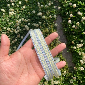 May include: Two flexible LED light strips with closely spaced white lights are held in an open hand. The strips are clear and appear to be made of a flexible material. The background is a field of green clover.
