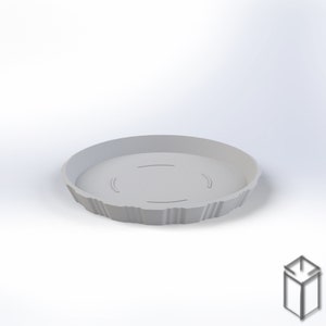 Puede incluir: Una bandeja redonda gris claro, impresa en 3D, con un borde texturizado y acanalado. La bandeja tiene tres hendiduras curvas en el interior. El producto est&aacute; dise&ntilde;ado para sujetar objetos. La bandeja se muestra sobre un fondo blanco.