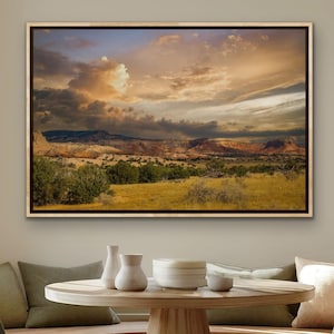May include: A rectangular landscape wall art print featuring a desert scene with golden yellow grasses in the foreground, green shrubs, and layered rocky mountains under a dramatic sky filled with soft orange, purple, and grey clouds at sunset.