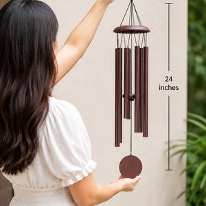 May include: A dark brown wind chime featuring six cylindrical metal tubes suspended from a circular wooden top, with a central striker and a round wind catcher at the bottom. The total length of the wind chime is marked as 24 inches.