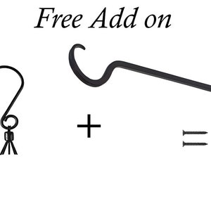 May include: A black metal S-hook with a small decorative tassel, a black metal wall-mounted plant bracket with a curved hook, and two black screws. The text "Free Add on" is displayed at the top, with a plus sign between the items.