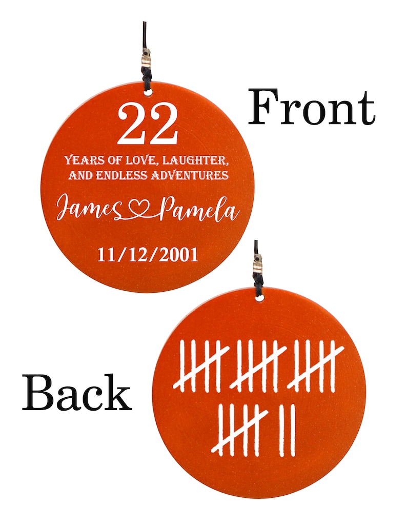 May include: A round, orange ornament with the number 22 and the text "YEARS OF LOVE, LAUGHTER, AND ENDLESS ADVENTURES." It also includes the names "James & Pamela" and the date 11/12/2001. The back has tally marks.