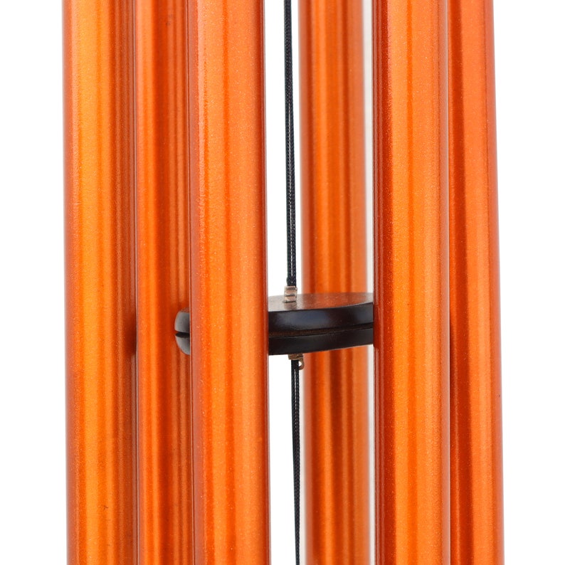 May include: Close-up of a wind chime with several vertical, orange-colored tubes. The tubes are suspended from a black disc and connected by black cords. The wind chime is designed to produce a pleasant sound when the wind blows.