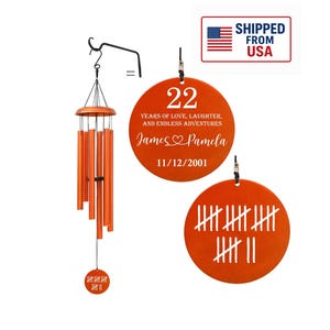 May include: Orange wind chimes with a wooden top and six orange tubes. Two orange circular ornaments display the number 22, names, and a date. The other ornament shows tally marks.