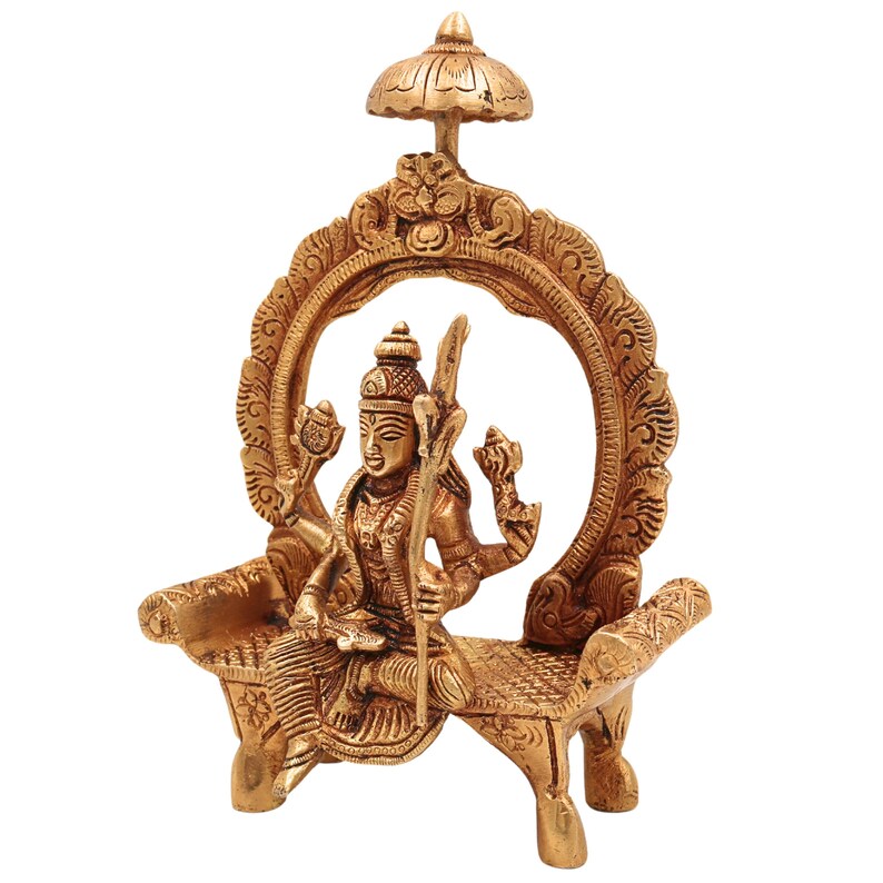 Puede incluir: Una detallada estatua de lat&oacute;n de una deidad sentada en un banco decorativo, enmarcada por un arco ornamentado y coronada por un peque&ntilde;o paraguas. La estatua presenta m&uacute;ltiples brazos y tallas intrincadas, mostrando el arte religioso tradicional.