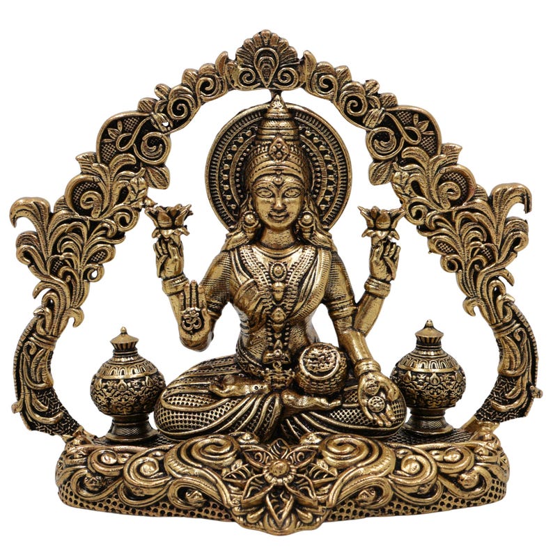 Op de afbeelding: Een gedetailleerd bronzen beeld van een zittende godheid, versierd met ingewikkelde sieraden en lotusbloemen. Het beeld wordt omlijst door een sierlijke boog en rust op een decoratieve basis, die traditionele kunstzinnigheid toont.