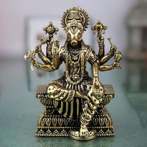 May include: A detailed bronze-colored statue of a deity with multiple arms and a boar's head. The figure is seated on an ornate base, adorned with intricate carvings and jewelry. The statue's pose is serene, with one hand raised in a blessing gesture.
