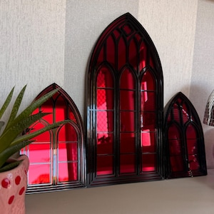 Pode incluir: Tr&ecirc;s pe&ccedil;as de decora&ccedil;&atilde;o de parede em estilo g&oacute;tico com molduras pretas e vidro vermelho vibrante. As janelas arqueadas variam em tamanho, criando uma exibi&ccedil;&atilde;o visualmente interessante. O vidro vermelho reflete a luz.