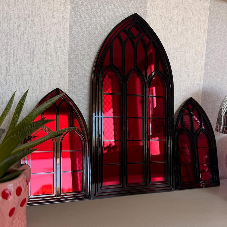Pode incluir: Tr&ecirc;s pe&ccedil;as de decora&ccedil;&atilde;o de parede em estilo g&oacute;tico com molduras pretas e vidro vermelho vibrante. As janelas arqueadas variam em tamanho, criando uma exibi&ccedil;&atilde;o visualmente interessante. O vidro vermelho reflete a luz.