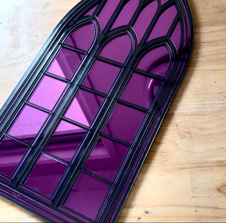 Pode incluir: Um espelho decorativo em forma de janela g&oacute;tica, com moldura preta e vidro espelhado roxo vibrante. O topo arqueado e os pain&eacute;is retangulares criam um efeito visual marcante. O espelho foi concebido para ser montado na parede.