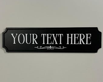 May include: Black rectangular sign with rounded edges and a decorative scroll design. The sign says "YOUR TEXT HERE" in white lettering.