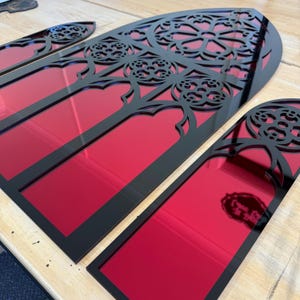 May include: Three arched wall panels featuring a black frame with intricate gothic-style cutouts layered over a reflective red surface. The panels vary in size, with a large central piece and two smaller side pieces, all displaying detailed patterns.