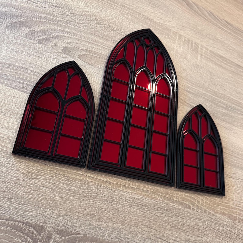 Pode incluir: Tr&ecirc;s decora&ccedil;&otilde;es de janelas em estilo g&oacute;tico com moldura preta e vidro vermelho. As janelas s&atilde;o de tamanhos variados, sendo a maior ao centro. O design lembra a arquitetura das catedrais.