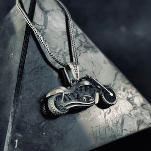 May include: A silver motorcycle pendant necklace with a detailed design. The pendant is hanging from a silver chain.