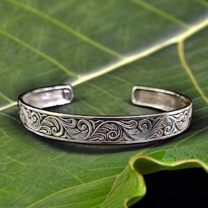 May include: A silver bangle bracelet with a detailed floral design. The bracelet is smooth and shiny, and the floral pattern is intricate and elegant.