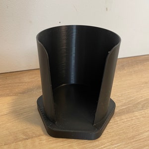 May include: A black plastic cup holder with a hexagonal base. The holder is designed to hold a single cup.