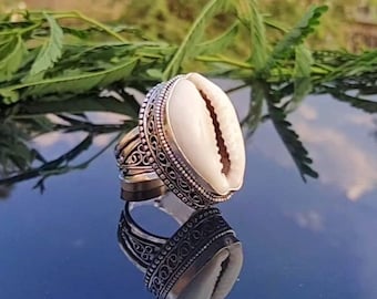 May include: A silver ring with a white cowrie shell set in a decorative filigree design.