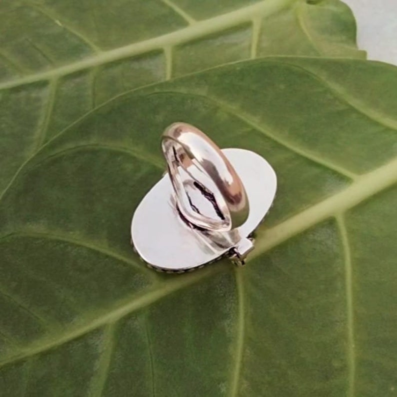 May include: Silver ring with an oval-shaped stone setting. The ring is shown from the back, revealing the smooth silver band and the open back of the setting.
