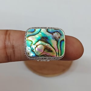 May include: A silver ring with a square abalone shell inlay. The shell has iridescent green, blue, and purple colors.