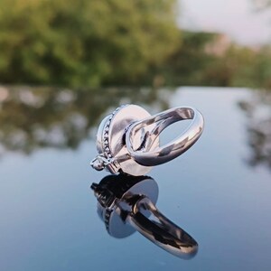 May include: A silver ring with a round, decorative stone set in the center. The ring is designed to spin freely.