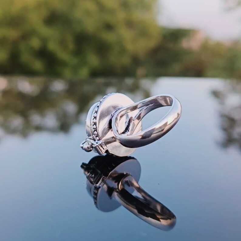 May include: A silver ring with a round, decorative stone set in the center. The ring is designed to spin freely.