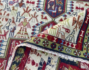 May include: A woven rug featuring a cream-colored field with a repeating pattern of stylized birds and animals in red, blue, green, and brown. The rug has a decorative border with floral motifs and a folded corner revealing a white fringed edge.