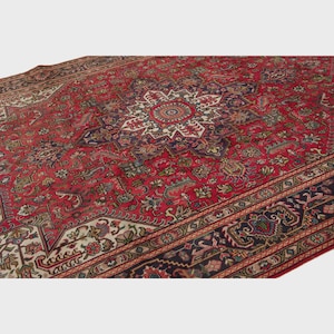 May include: A large, ornate red rug with a central medallion design and intricate floral patterns. The rug features a border with dark blue and cream accents, showcasing a traditional Persian style. The rug's detailed design and rich colors create a luxurious feel.