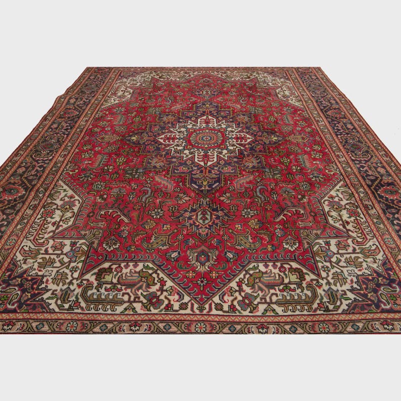 May include: A large, rectangular red rug with an intricate, symmetrical pattern. The rug features a central medallion design in cream, navy, and burgundy, surrounded by detailed floral and geometric motifs. The border is a dark navy with repeating patterns.