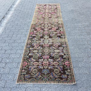 May include: A rectangular, vintage-style runner rug with an intricate floral pattern. The rug features a dark brown base with accents of pink, blue, and green. The rug is placed on a gray stone surface.