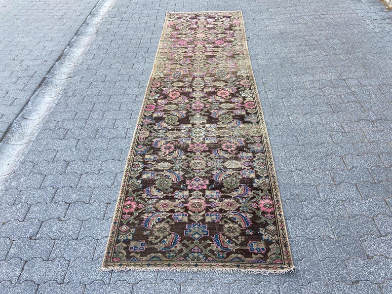 May include: A rectangular, vintage-style runner rug with an intricate floral pattern. The rug features a dark brown base with accents of pink, blue, and green. The rug is placed on a gray stone surface.