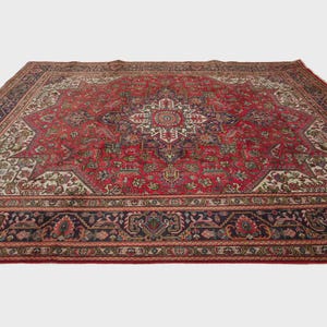 May include: A large, rectangular area rug with a central medallion design. The rug features a predominantly red field with intricate patterns in navy, cream, and other colors. The border is a dark navy with floral motifs.