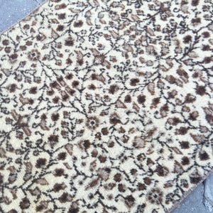 May include: A cream-colored rug with a brown floral pattern. The rug has a soft, fuzzy texture.