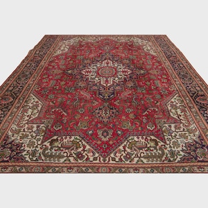 May include: A large, rectangular red rug with an intricate, symmetrical pattern. The rug features a central medallion design in cream, navy, and burgundy, surrounded by detailed floral and geometric motifs. The border is a dark navy with repeating patterns.