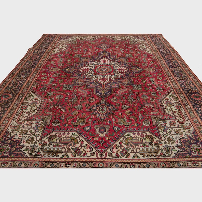 May include: A large, rectangular red rug with an intricate, symmetrical pattern. The rug features a central medallion design in cream, navy, and burgundy, surrounded by detailed floral and geometric motifs. The border is a dark navy with repeating patterns.
