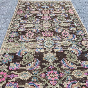 May include: A rectangular, vintage rug with a dark brown background and an intricate pattern. The design features floral and geometric elements in shades of pink, blue, and green. The rug has a distressed look, suggesting age and use.