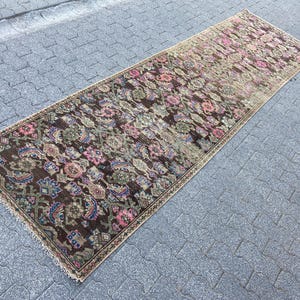 May include: A long, rectangular rug with a floral pattern in shades of brown, pink, blue, and green. The rug has a distressed, vintage look, with a faded appearance. The edges are fringed.