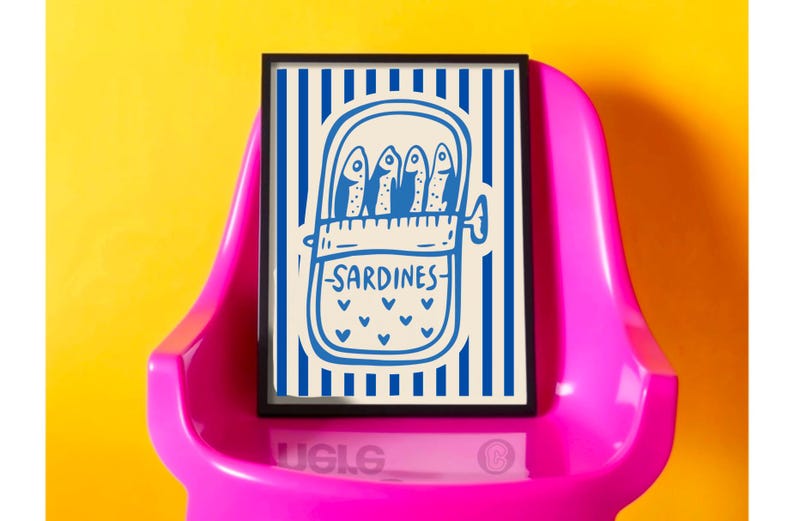 Puede incluir: Una impresi&oacute;n art&iacute;stica enmarcada con una ilustraci&oacute;n azul y blanca de sardinas enlatadas. La obra de arte presenta un fondo a rayas y la palabra "Sardines" escrita debajo. La impresi&oacute;n se muestra en una silla rosa sobre un fondo amarillo.