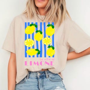 Puede incluir: Camiseta beige con un gr&aacute;fico de lim&oacute;n. El dise&ntilde;o presenta limones amarillos con hojas verdes y rayas azules, con el texto "La vita al LIMONE" en rosa. La camiseta es de estilo casual.