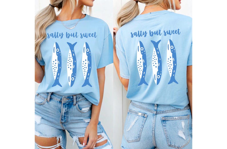 Puede incluir: Camiseta azul claro con la frase "salty but sweet" y un dise&ntilde;o de tres peces azules y blancos. El mismo dise&ntilde;o est&aacute; en la parte delantera y trasera. La modelo lleva unos shorts vaqueros azules claros.