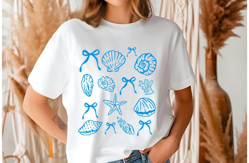 May include: White t-shirt with a blue seashell and starfish design. The design includes various seashells, starfish, and coral.