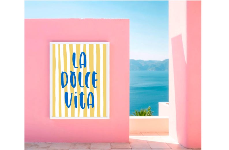 Puede incluir: Una impresi&oacute;n art&iacute;stica enmarcada con las palabras "LA DOLCE VITA" en escritura azul sobre un fondo a rayas amarillas y blancas. La impresi&oacute;n est&aacute; montada en una pared rosa, con una vista del oc&eacute;ano y el cielo al fondo.