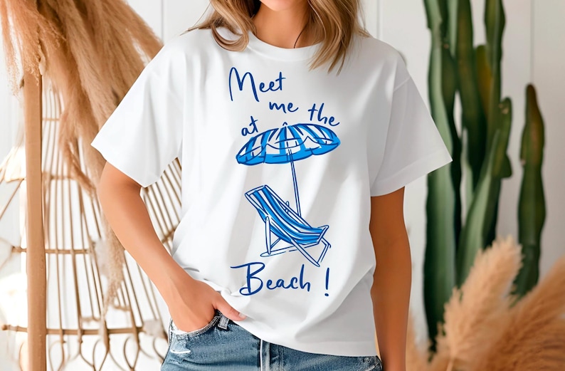 May include: White t-shirt with a blue graphic design that says "Meet me at the beach!" with a beach chair and umbrella.