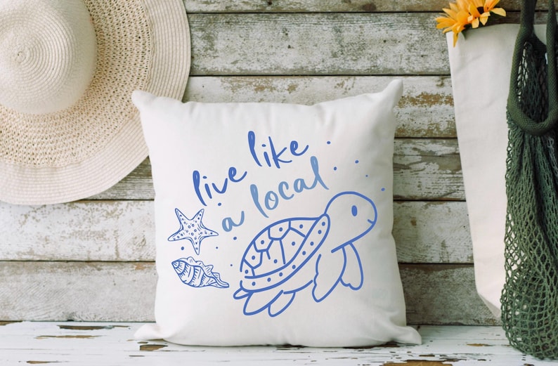 May include: White pillow with blue text that says "Live like a local."  The pillow also features a blue illustration of a sea turtle, a starfish, and a seashell.